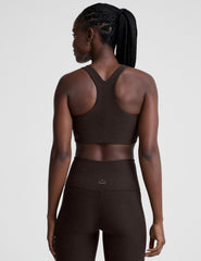 woman wearing a brown racerback bra and leggings on a plain background.