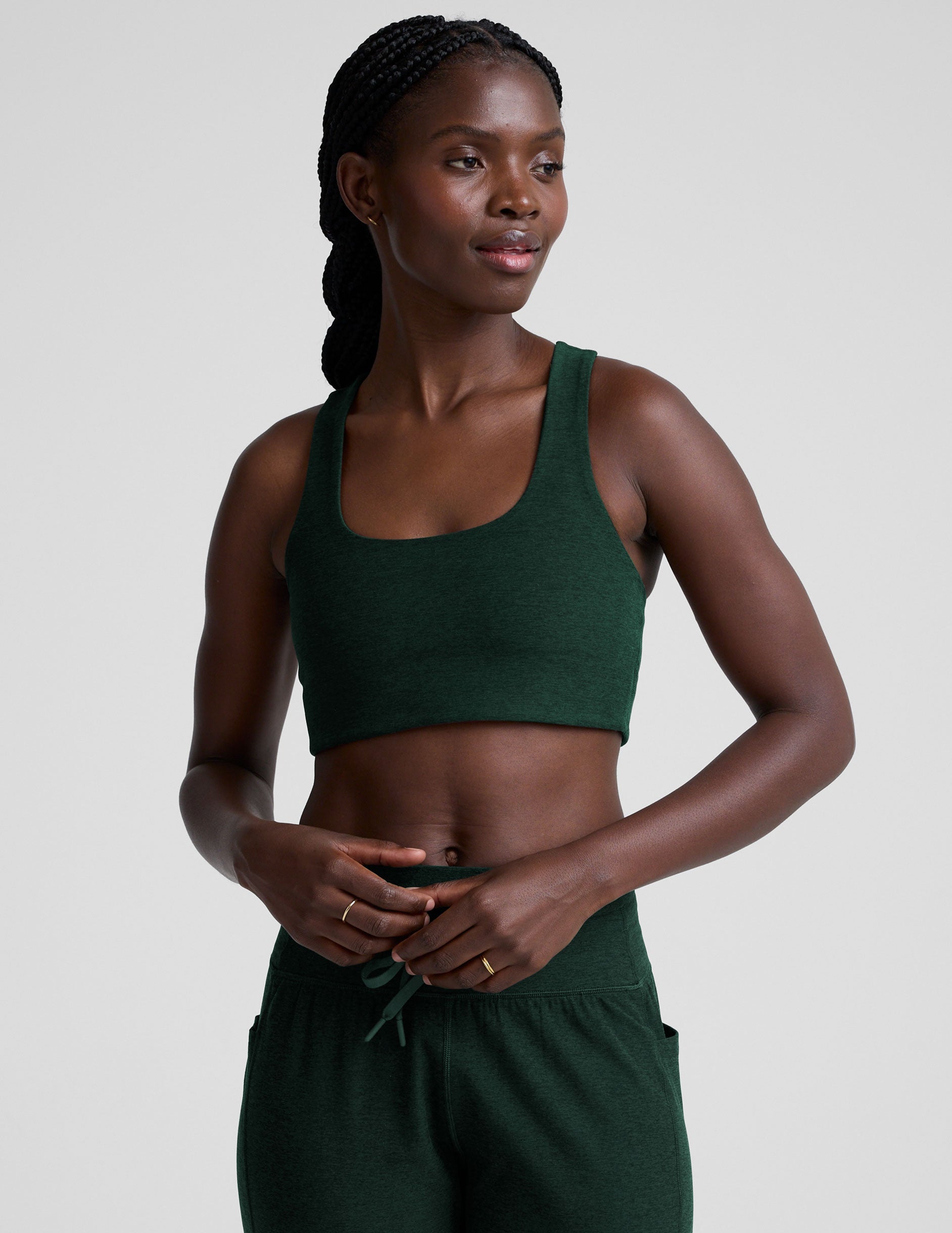 model wearing a green scoop neck racerback long line sports bra and joggers against a plain background.