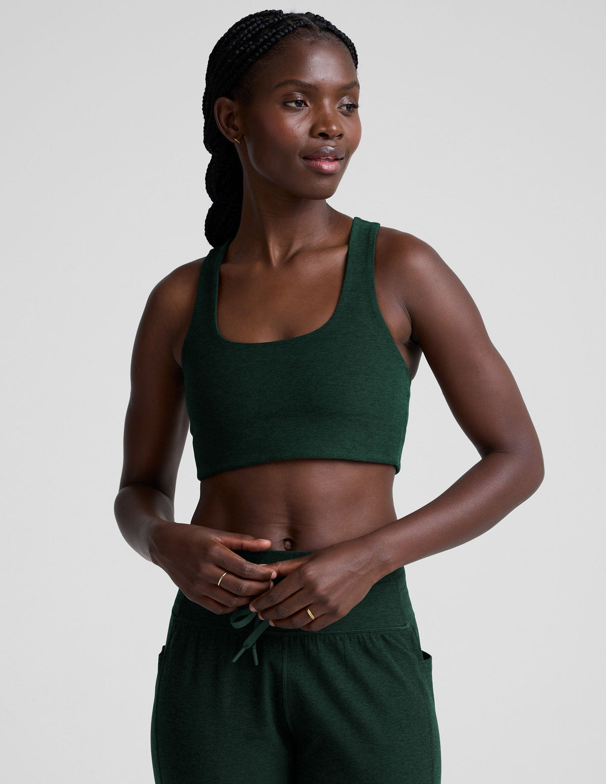 model wearing a green scoop neck racerback long line sports bra and joggers against a plain background.