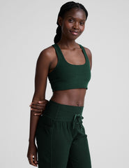 model wearing a green scoop neck racerback long line sports bra and joggers against a plain background.