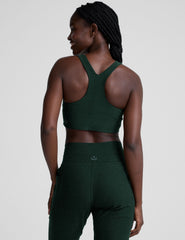 model wearing a green scoop neck racerback long line sports bra and joggers against a plain background.