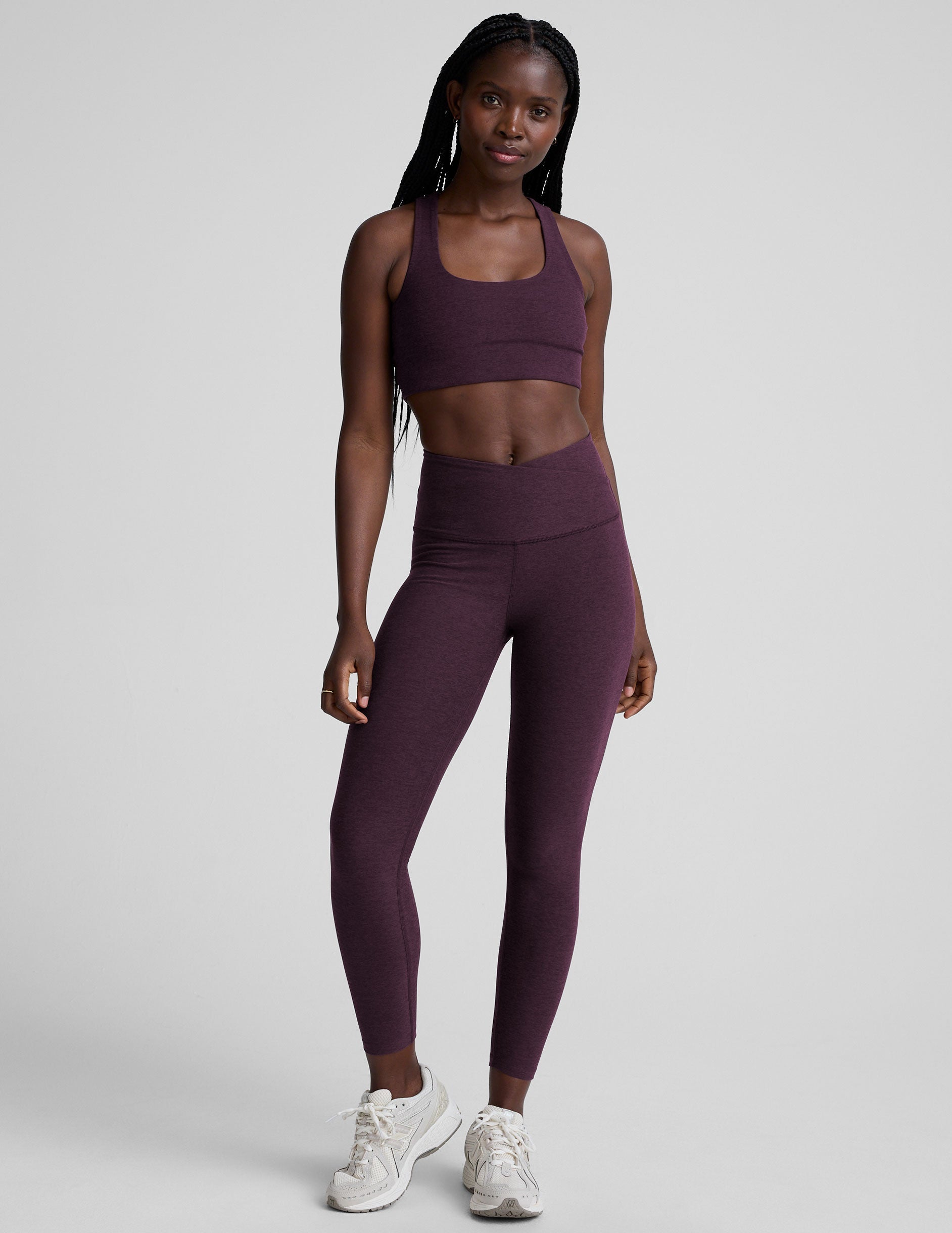 model wearing a purple scoop neck racerback long line sports bra and leggings set on a plain background.