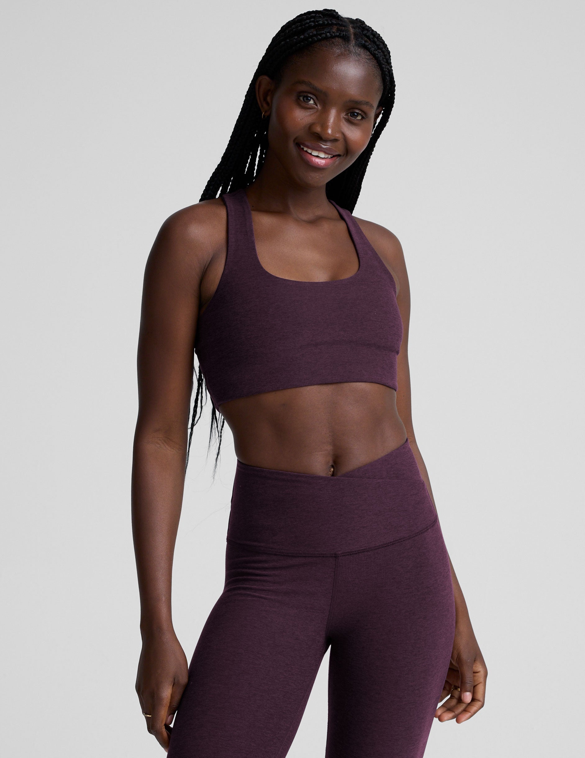 model wearing a purple scoop neck racerback long line sports bra and leggings set on a plain background.