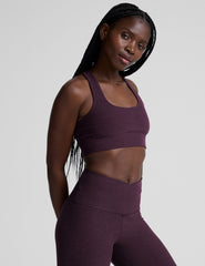 model wearing a purple scoop neck racerback long line sports bra and leggings set on a plain background.