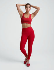 woman wearing a red scoop neck racerback bra and leggings on a plain background.