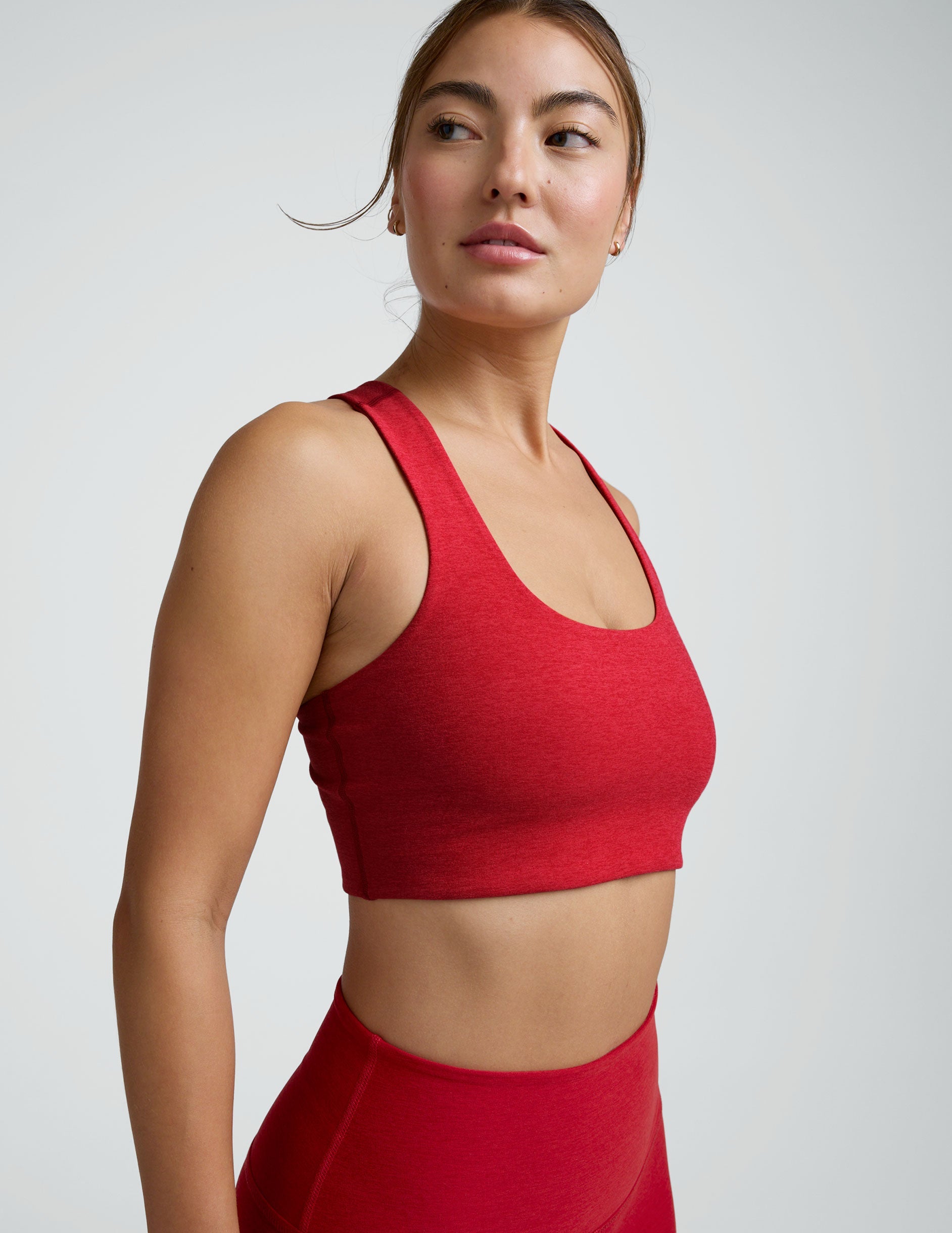 woman wearing a red scoop neck racerback bra and leggings on a plain background.