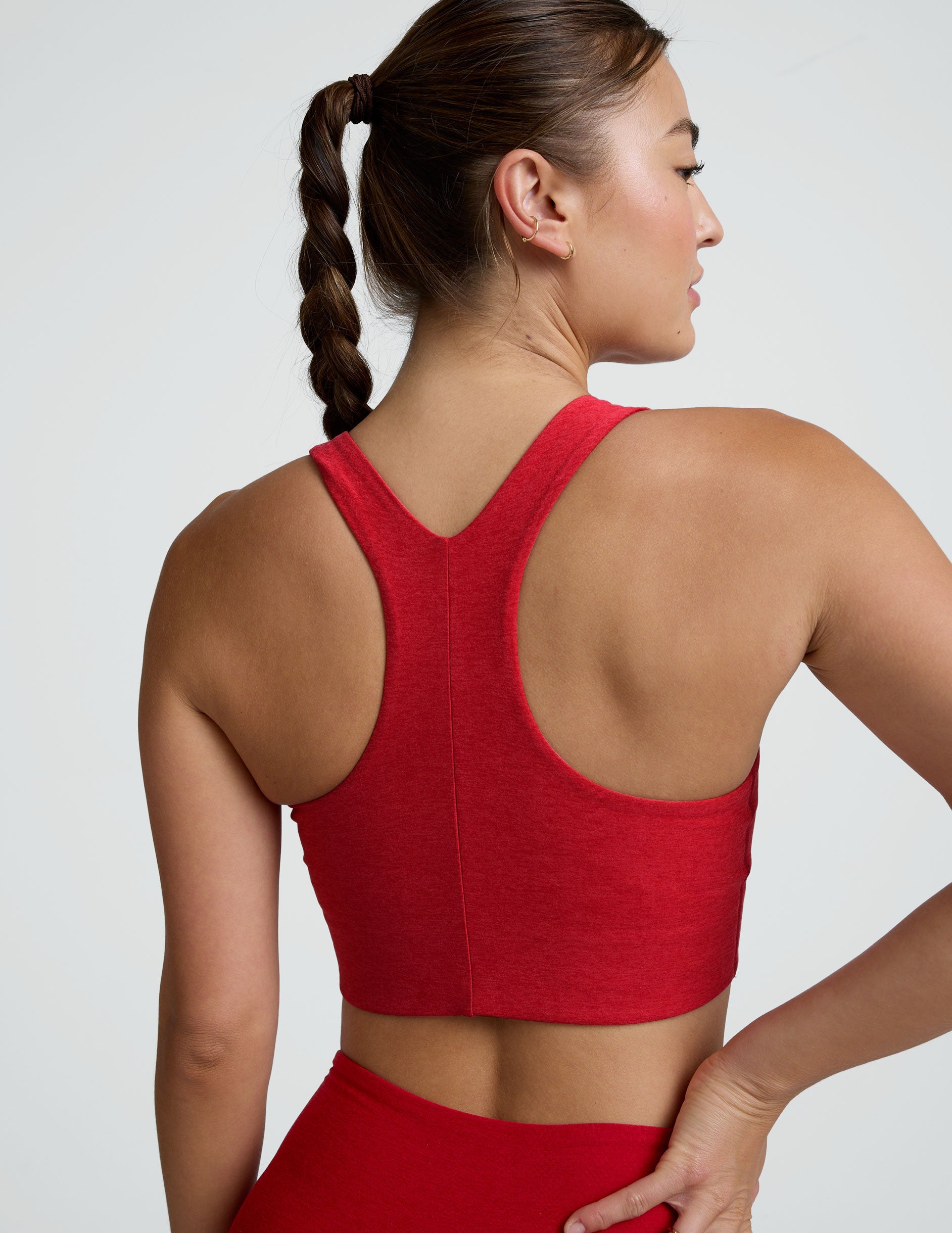 woman wearing a red scoop neck racerback bra and leggings on a plain background.