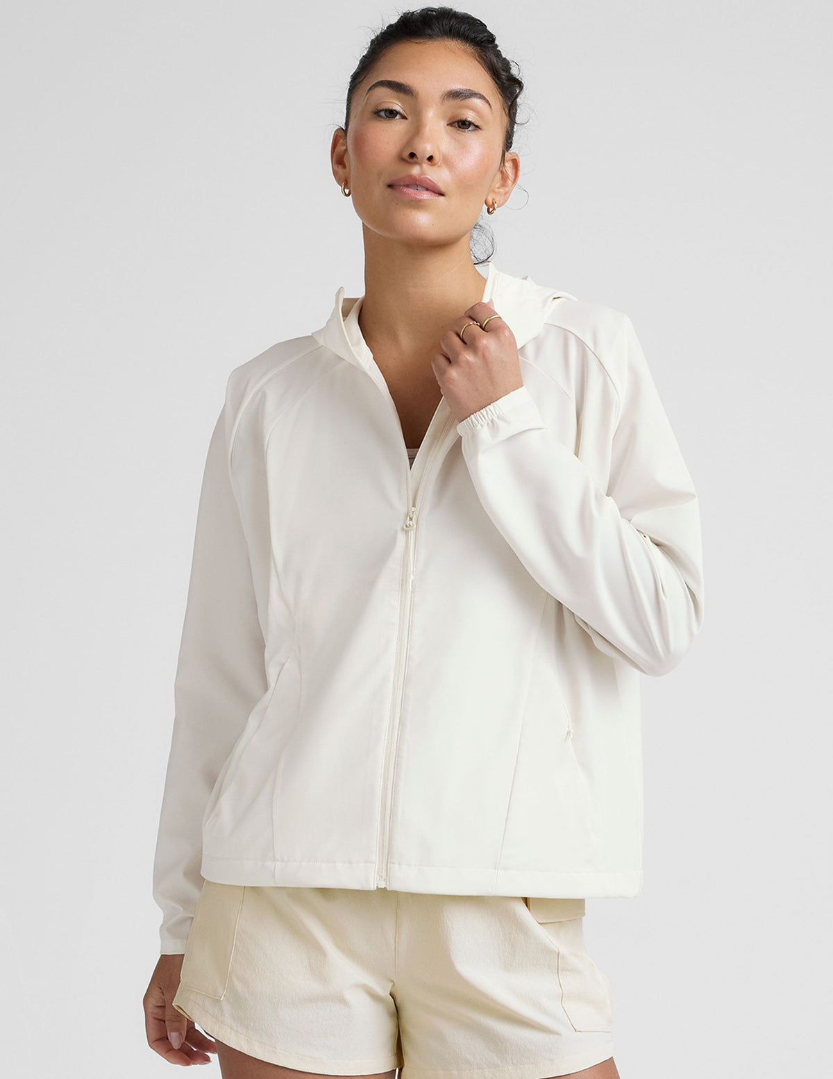 model wearing a white zip-up jacket with hood and shorts on a plain background.