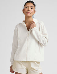 model wearing a white zip-up jacket with hood and shorts on a plain background.