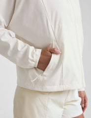 model wearing a white zip-up jacket with hood and shorts on a plain background.