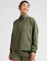 model is wearing an olive green zip-up jacket with side pockets and a hood on a white background.