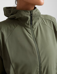 model is wearing an olive green zip-up jacket with side pockets and a hood on a white background.