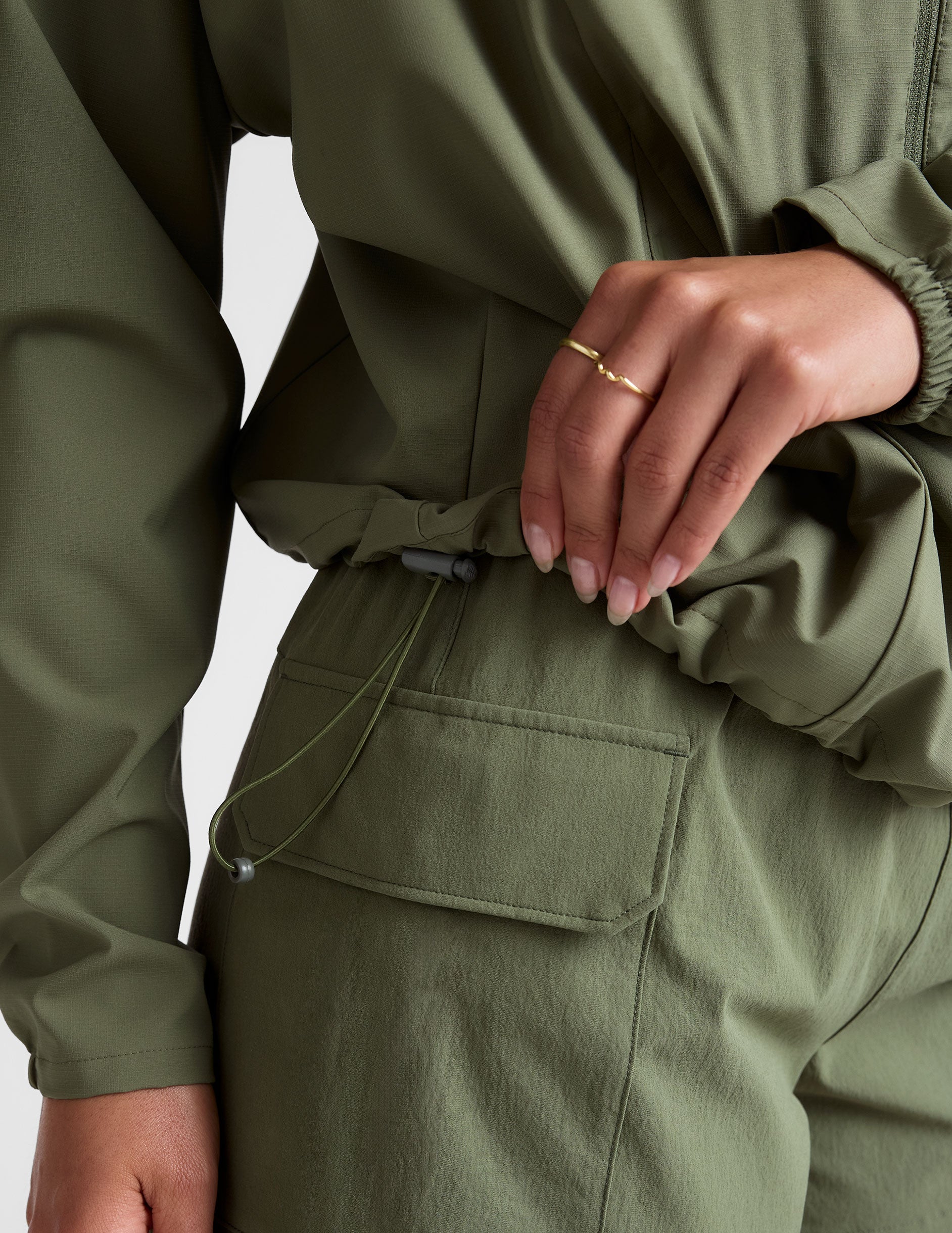 model is wearing an olive green zip-up jacket with side pockets and a hood on a white background.