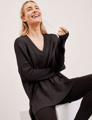 Woman wearing a brown sweater and black leggings against a plain background.