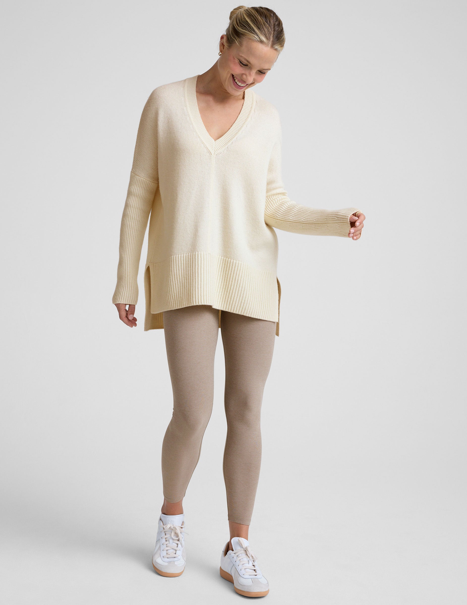 woman wearing a cream-colored v-neck sweater against a plain background.