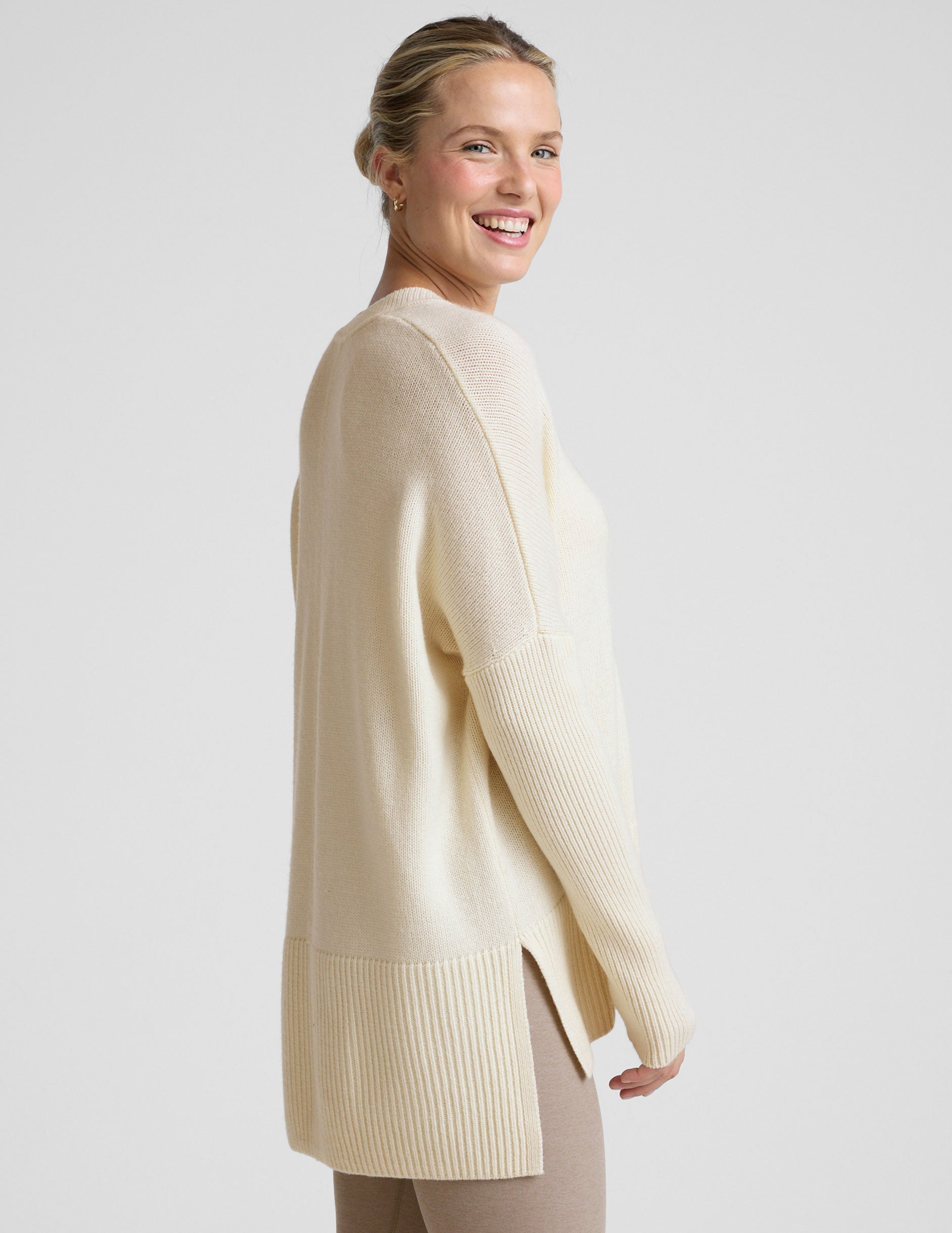 woman wearing a cream-colored v-neck sweater against a plain background.