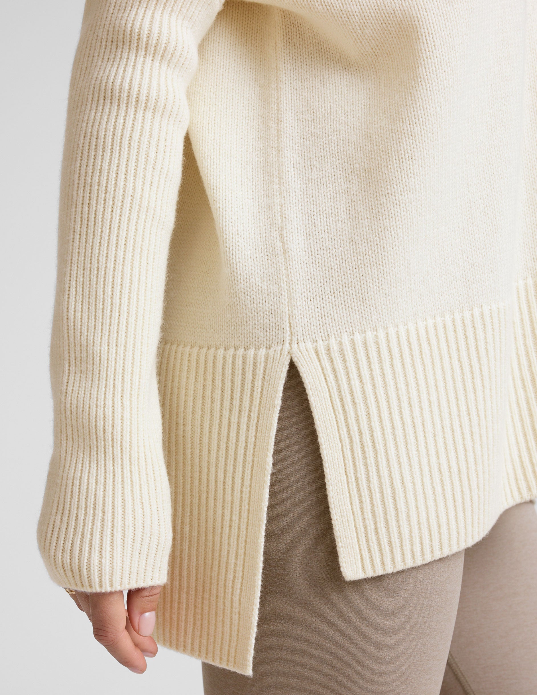 woman wearing a cream-colored v-neck sweater against a plain background.