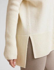 woman wearing a cream-colored v-neck sweater against a plain background.