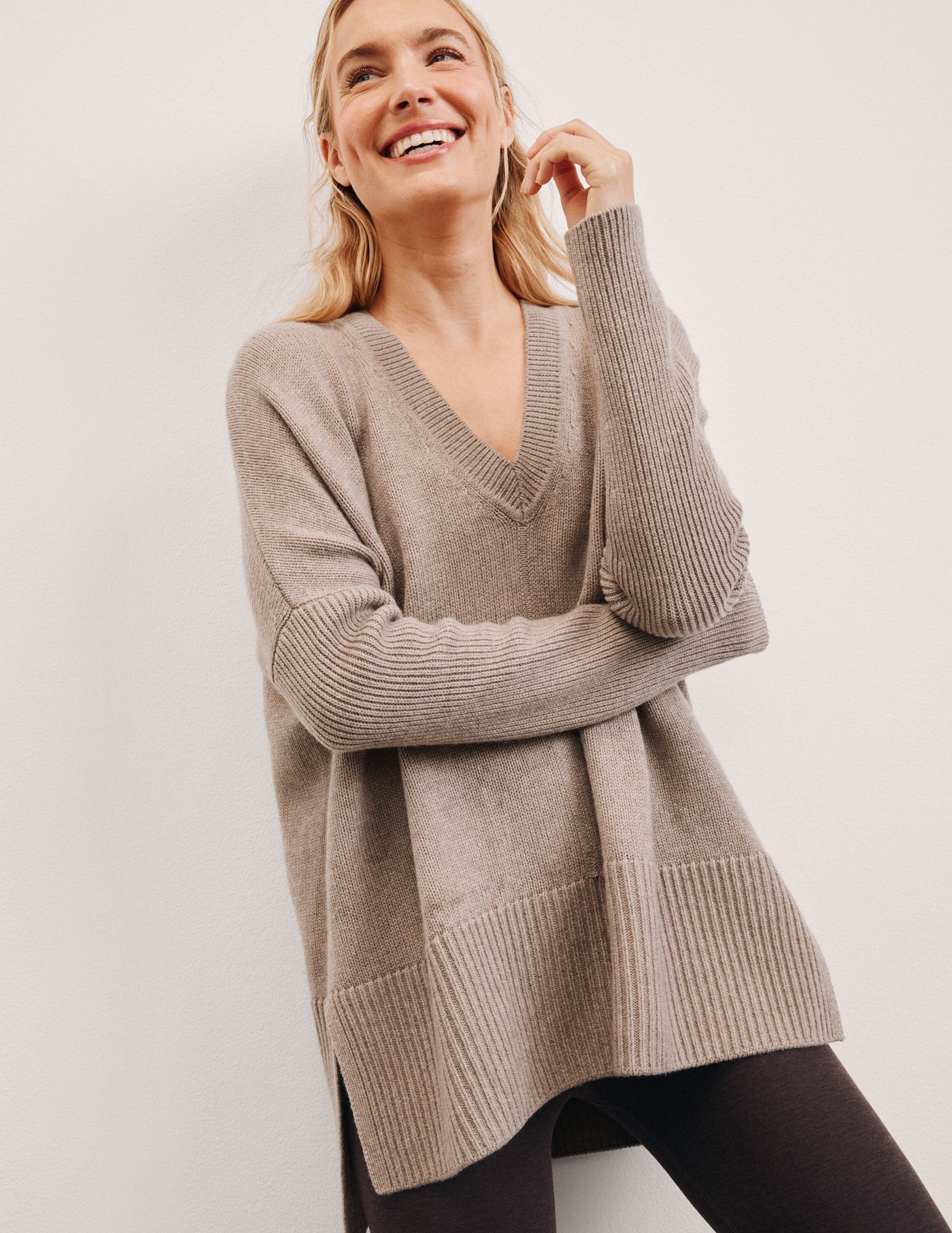 woman wearing a beige v-neck sweater against a plain background.