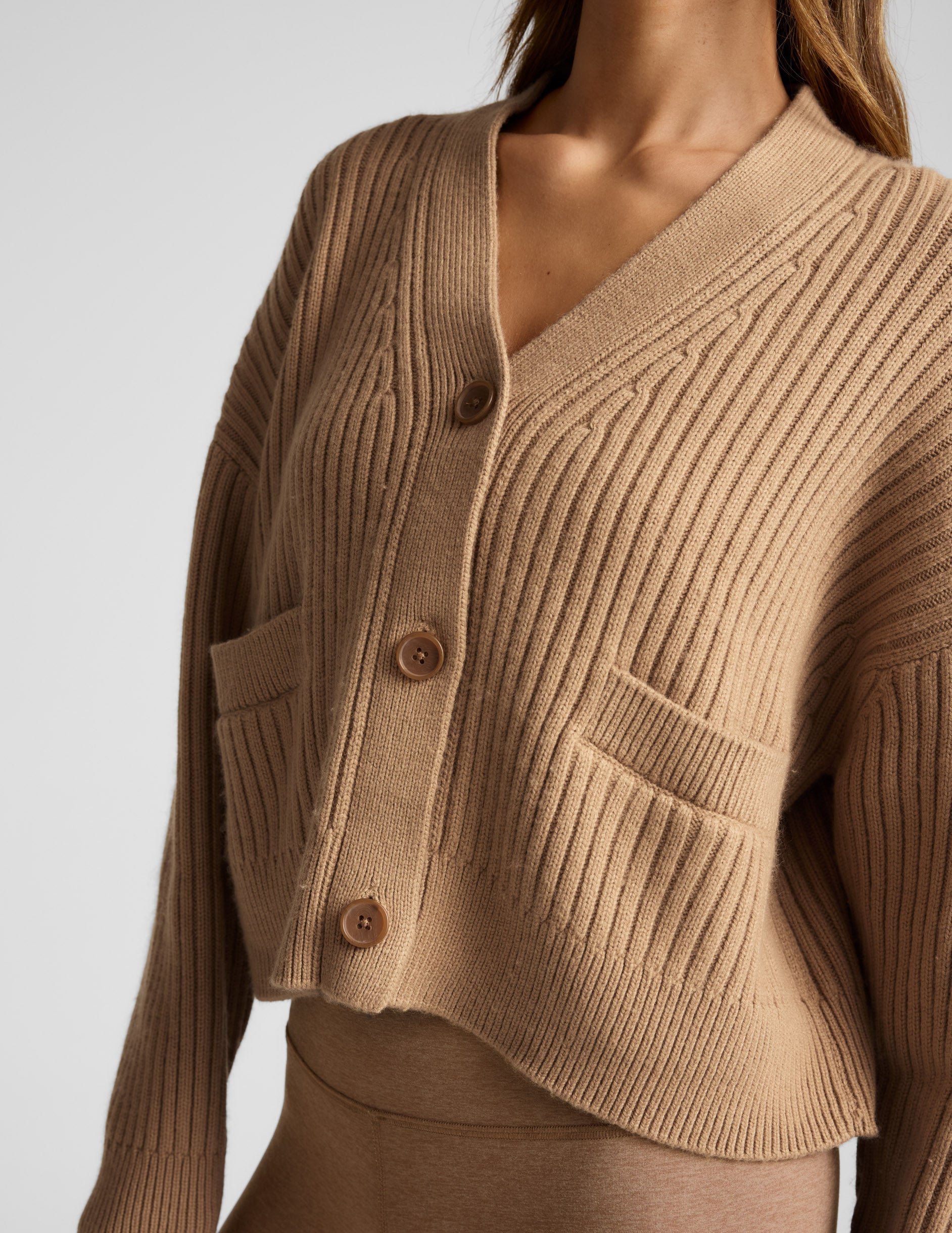 woman wearing a brown button up ribbed cardigan against a plain background.