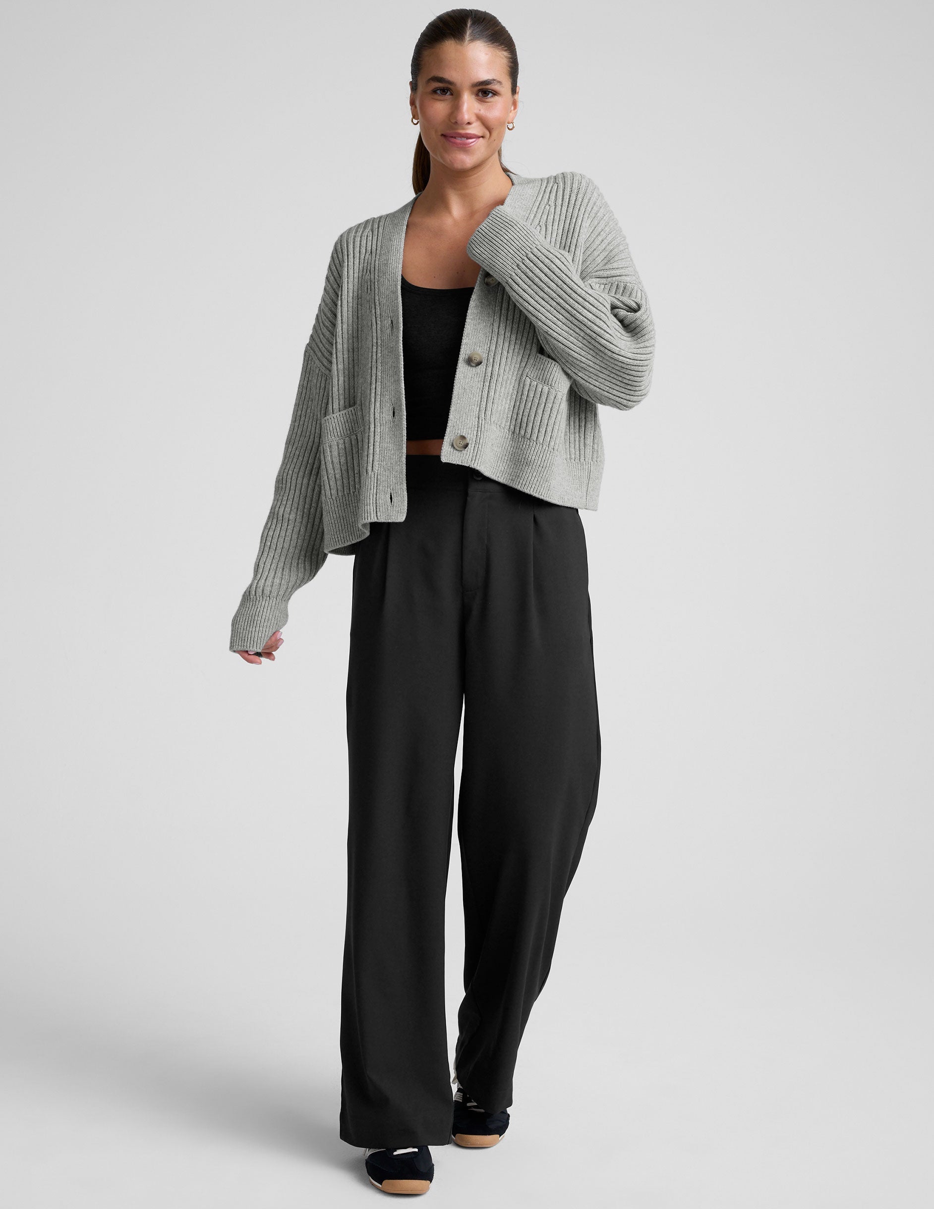 woman wearing a gray ribbed cardigan on a plain background.