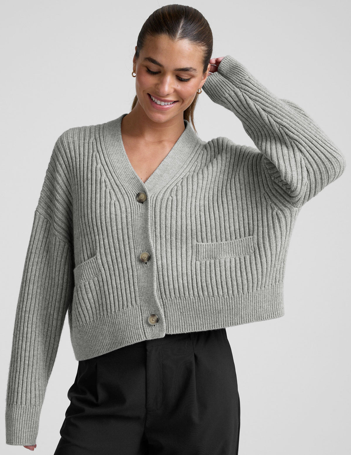 woman wearing a gray ribbed cardigan on a plain background.