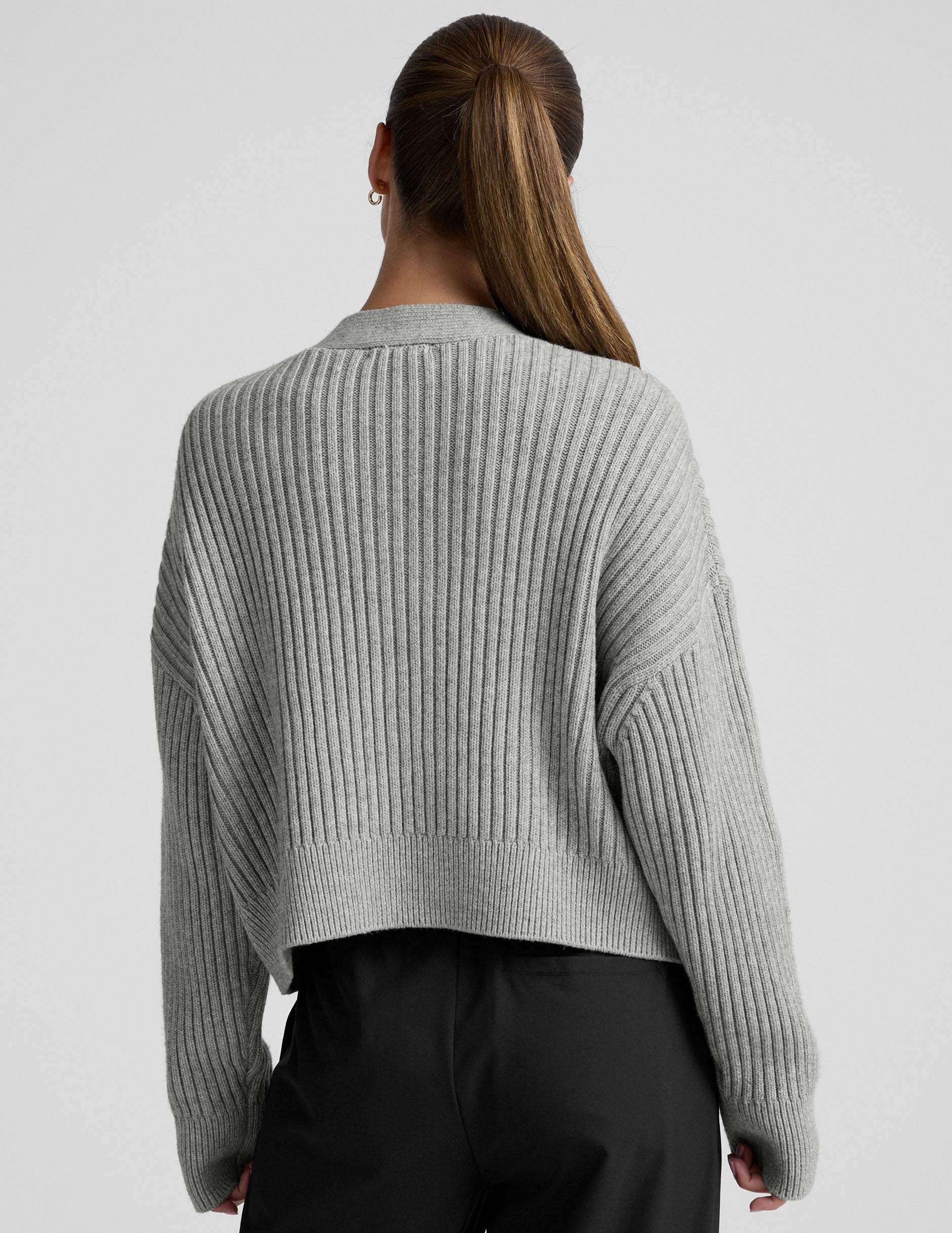 woman wearing a gray ribbed cardigan on a plain background.