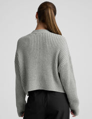 woman wearing a gray ribbed cardigan on a plain background.