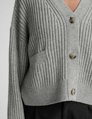 woman wearing a gray ribbed cardigan on a plain background.