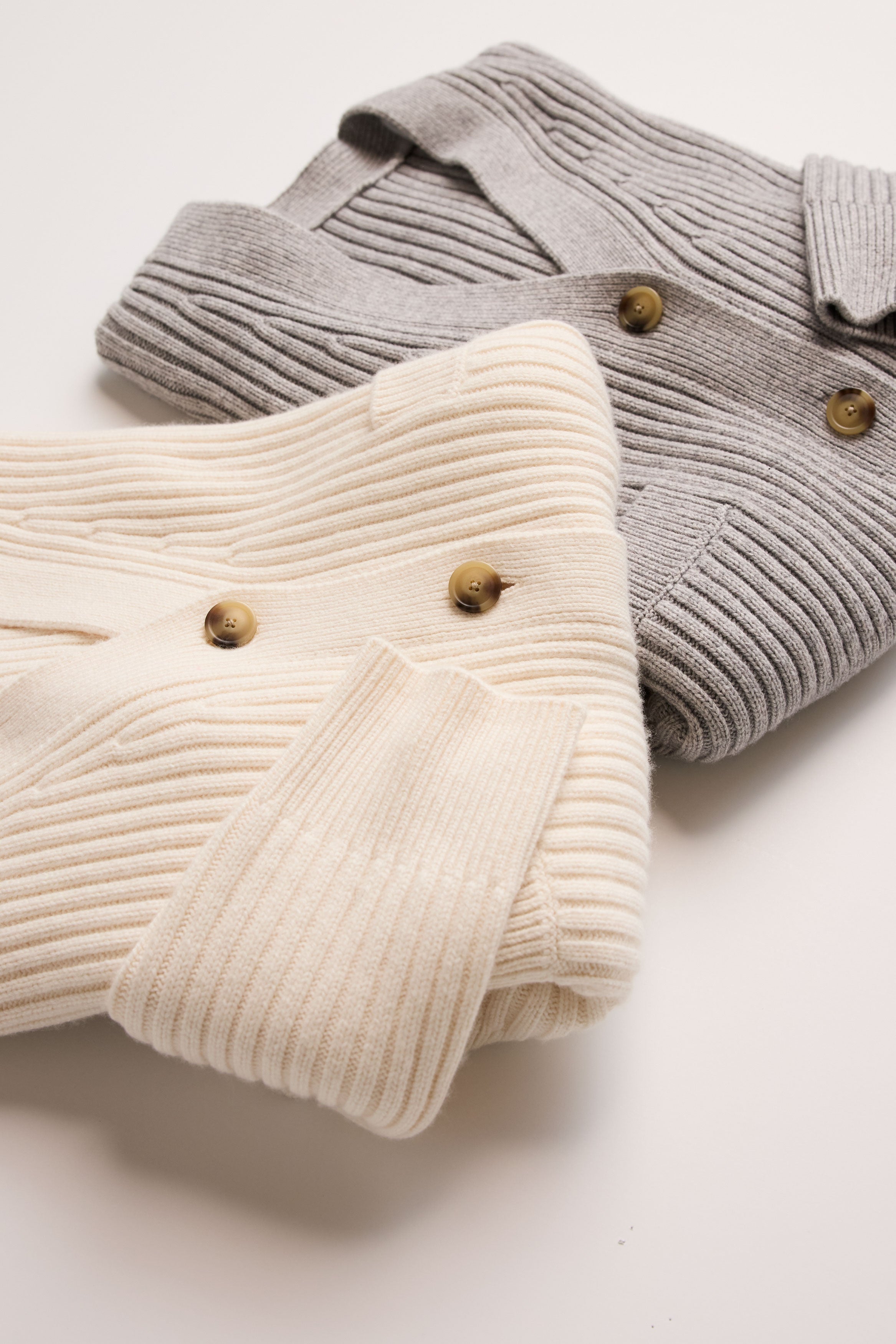 Two folded ribbed sweaters, one gray and one beige, on a light background.