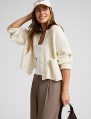 woman wearing a cream cardigan on a plain background.