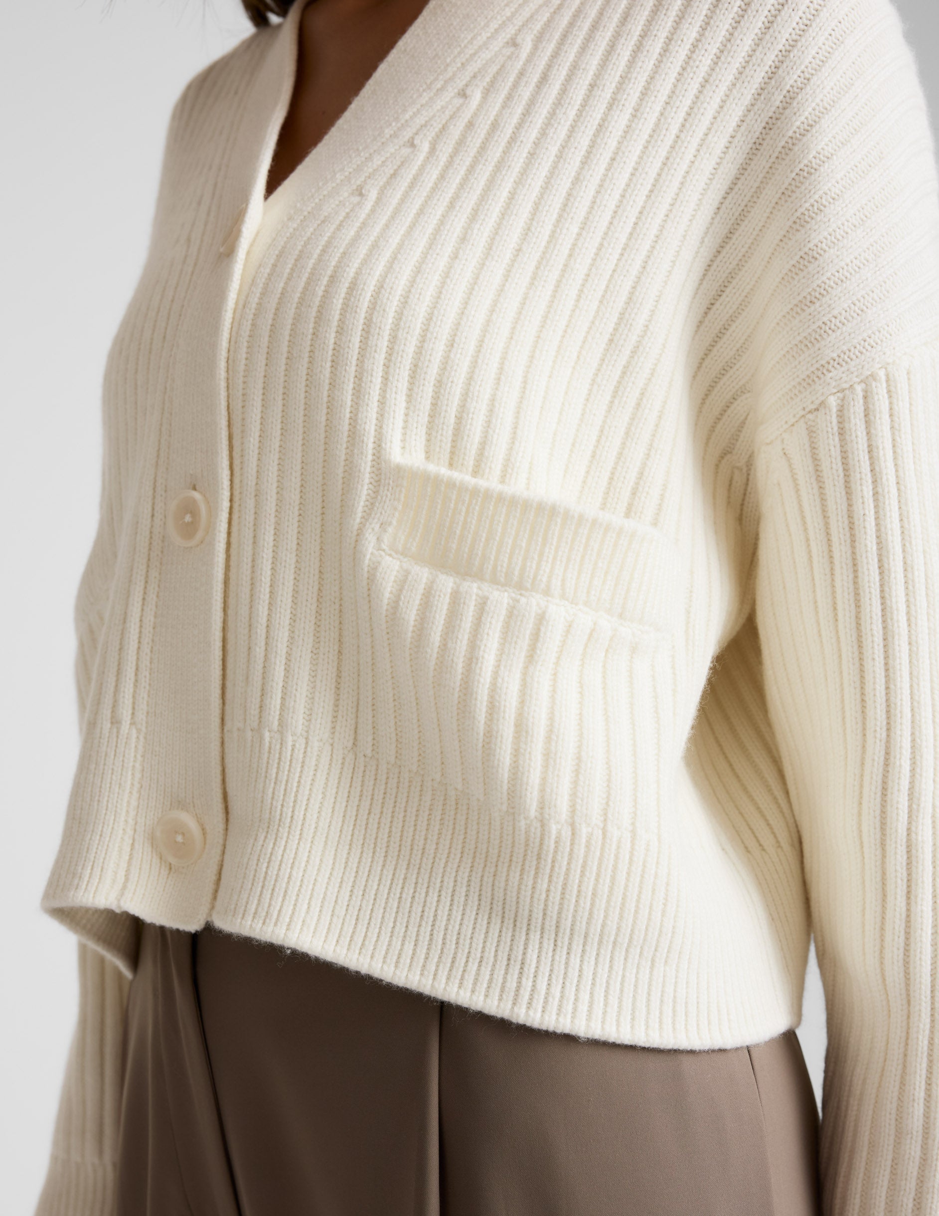 woman wearing a cream cardigan on a plain background.