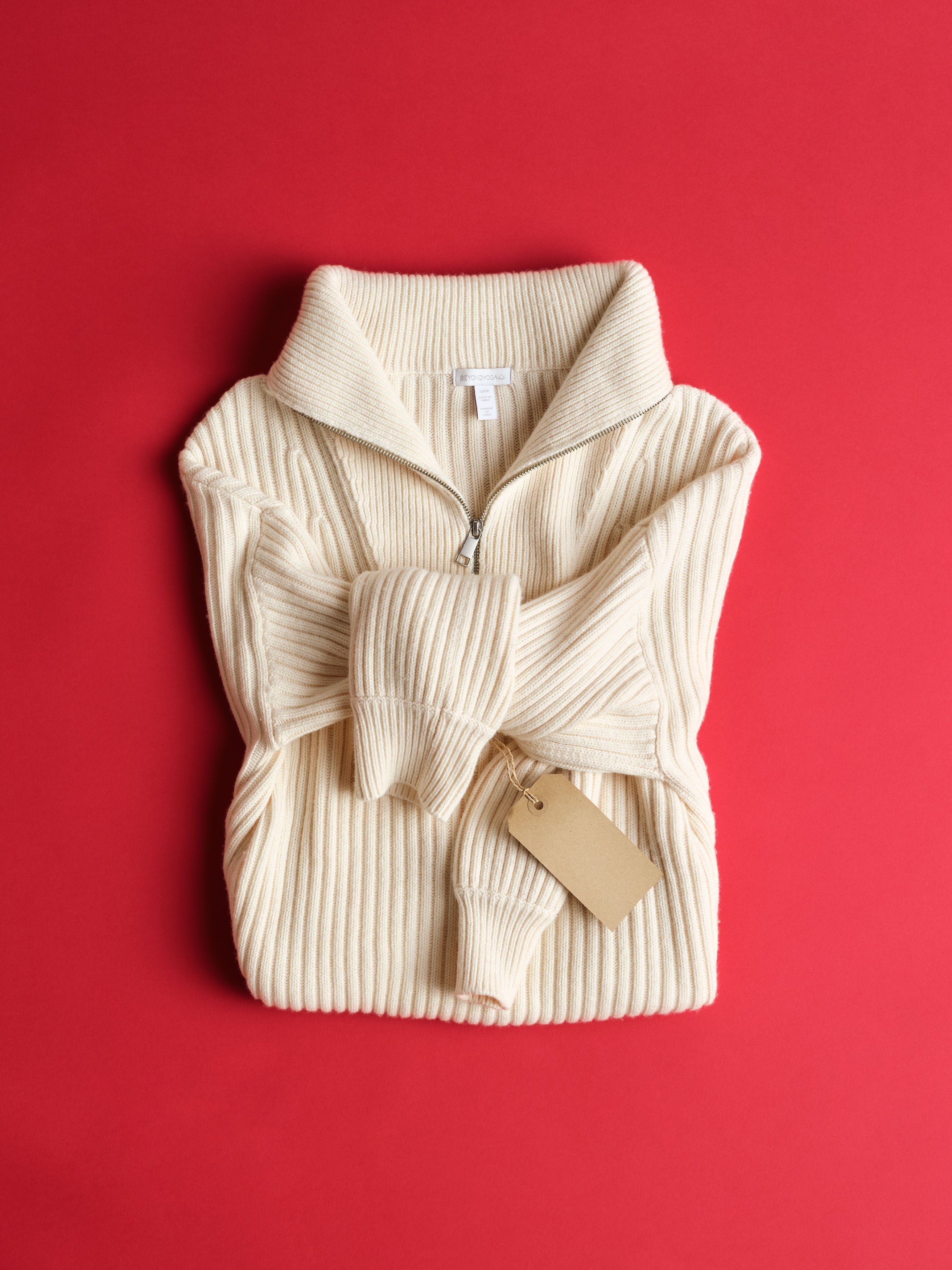 Folded cream ribbed sweater with a tag on a red background.