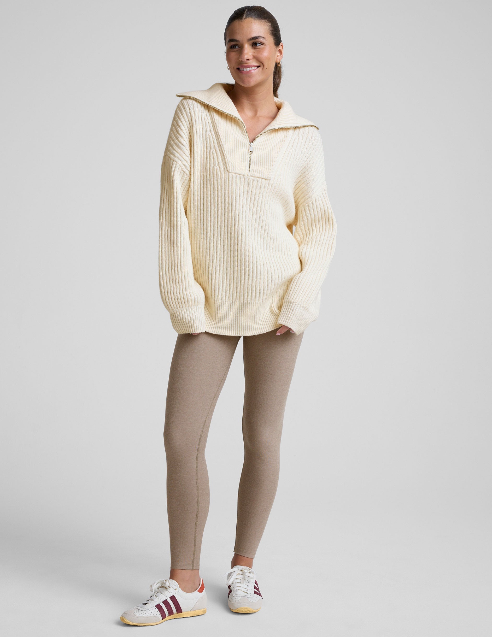 woman wearing a white quarter zip collared sweater against a plain background.