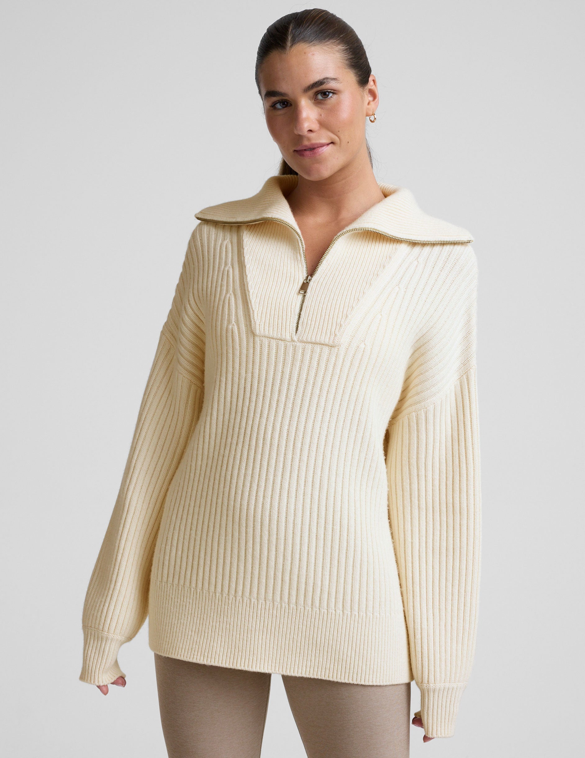 woman wearing a white quarter zip collared sweater against a plain background.