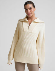 woman wearing a white quarter zip collared sweater against a plain background.