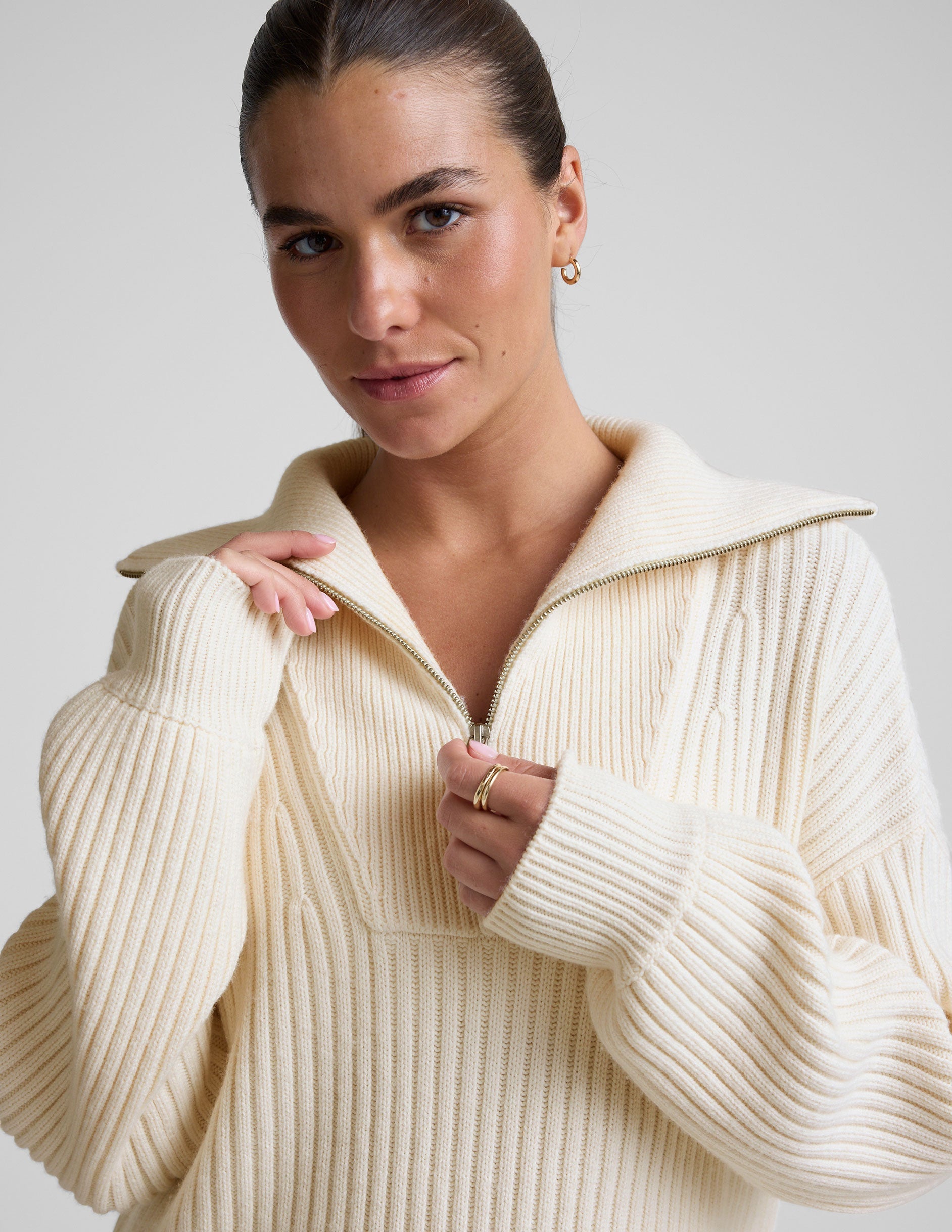 woman wearing a white quarter zip collared sweater against a plain background.
