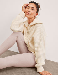 woman wearing a white quarter zip collared sweater against a plain background.