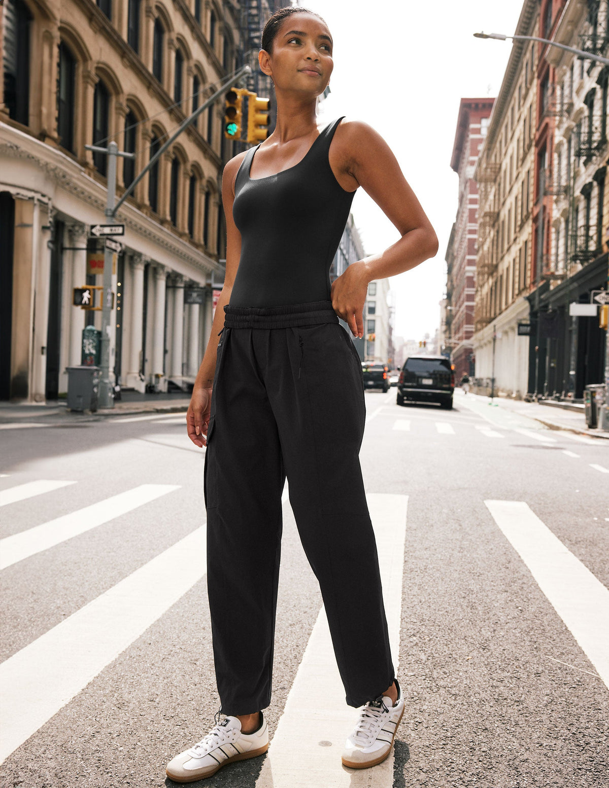 model in black bodysuit and black cargo style pants standing on a city street.