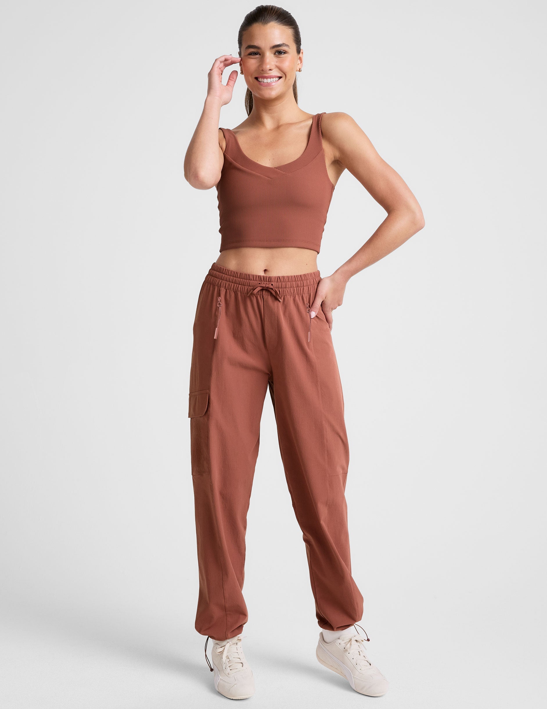 model wearing an orange ribbed tank top and orange cargo pants on a white background.