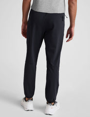 man wearing a gray crew neck t-shirt and blue joggers on a plain background.