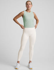 model wearing a blue sleeveless top and white pants on a plain background.