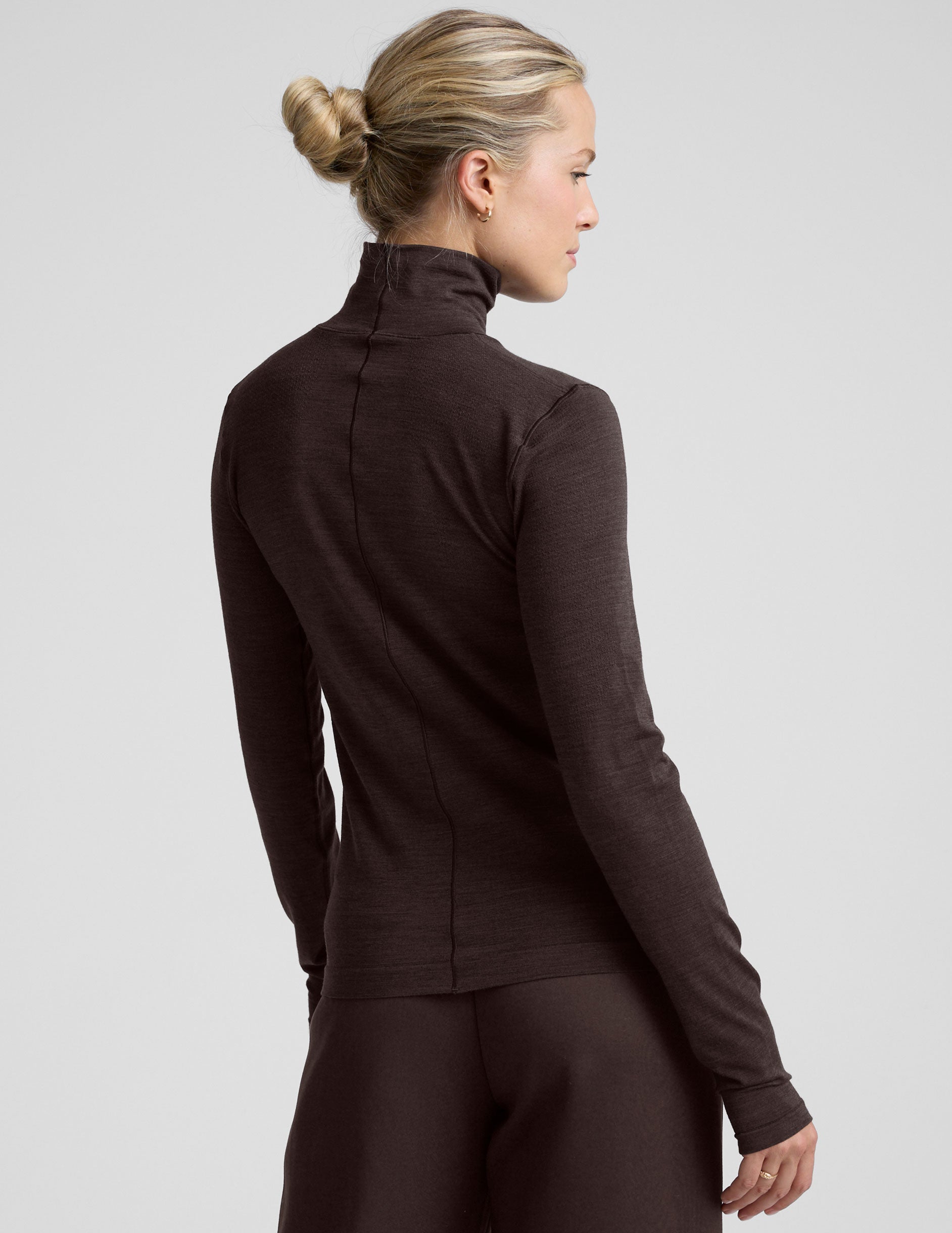 woman wearing a brown turtleneck and pants on a light gray background.