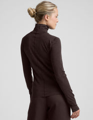 woman wearing a brown turtleneck and pants on a light gray background.