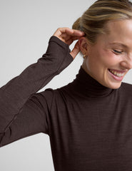 woman wearing a brown turtleneck and pants on a light gray background.