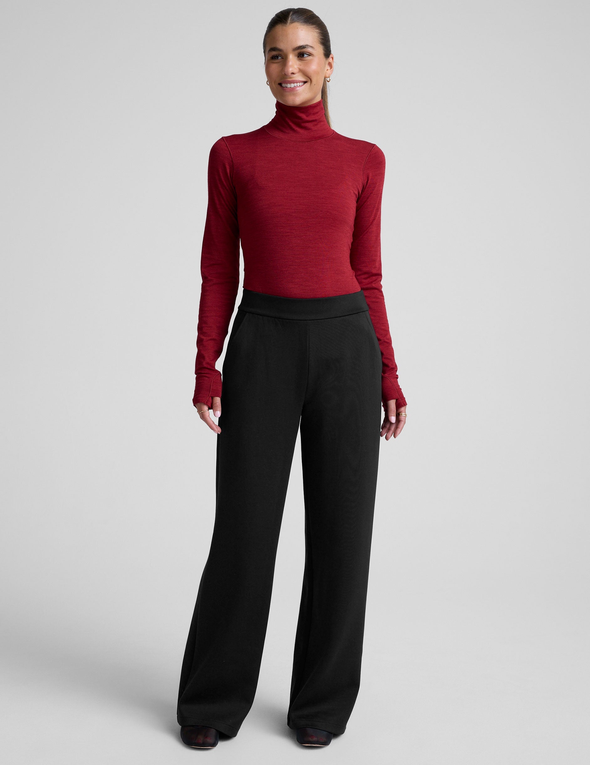 model wearing a red turtleneck long sleeve top and black pants on a plain background.
