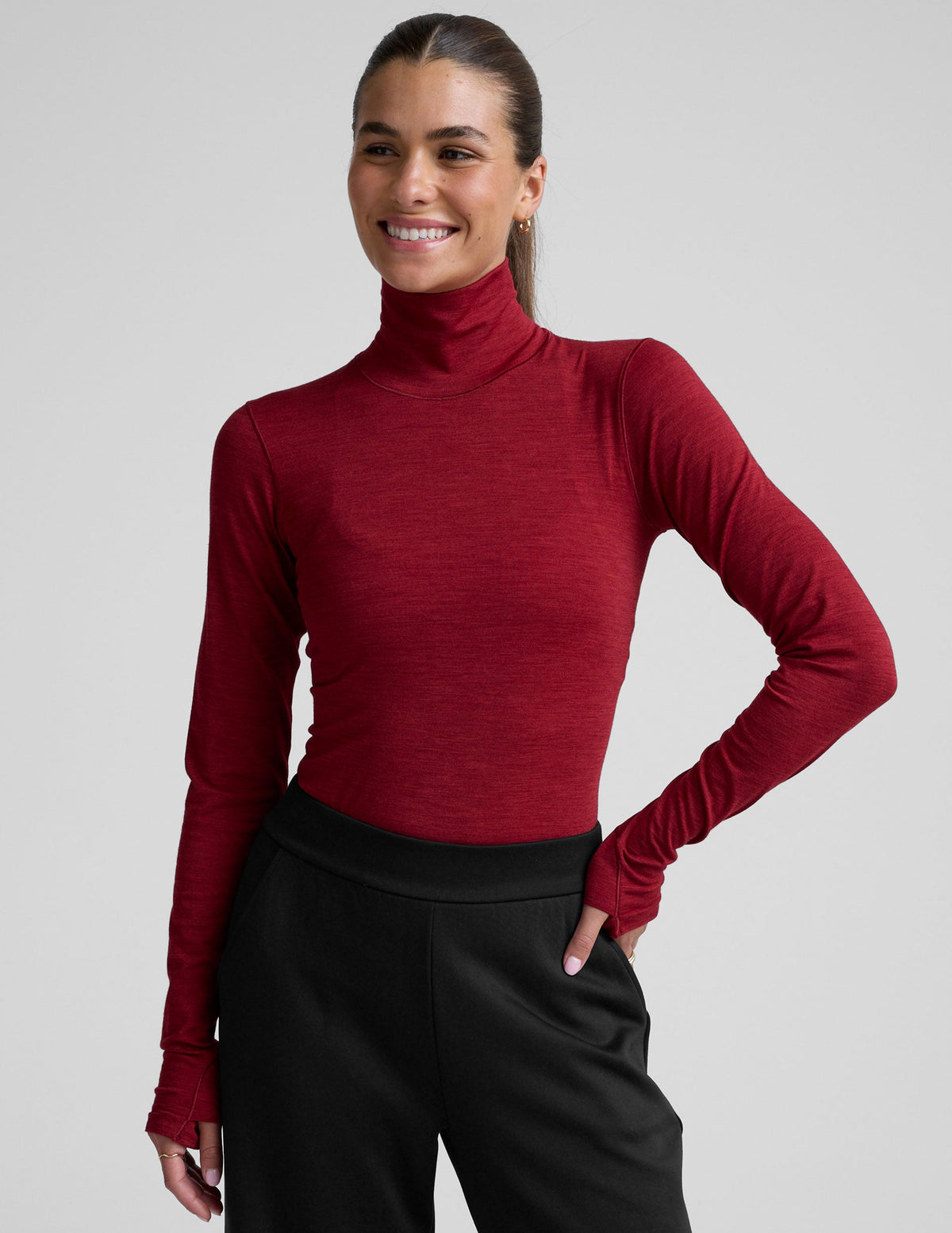 model wearing a red turtleneck long sleeve top and black pants on a plain background.