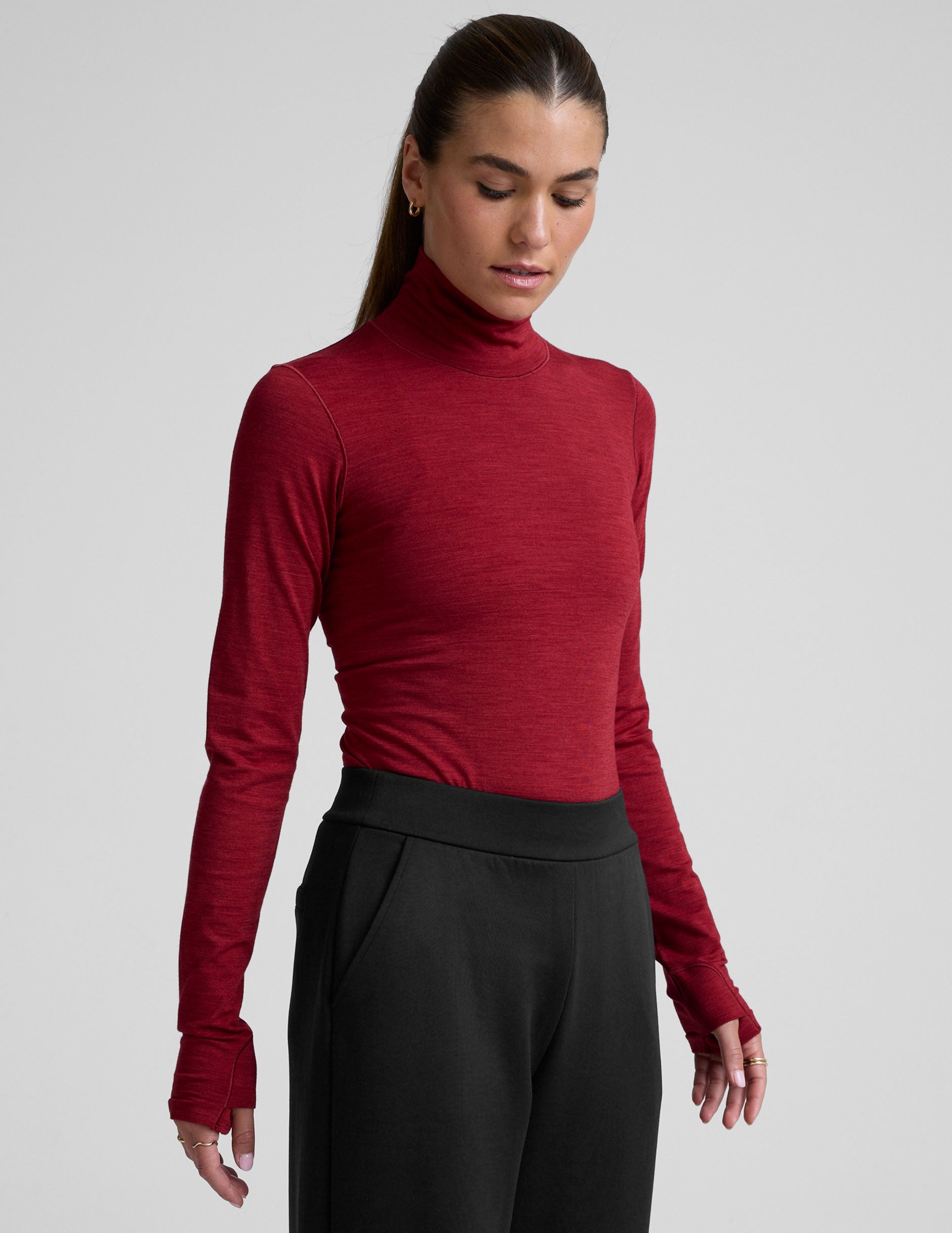 model wearing a red turtleneck long sleeve top and black pants on a plain background.