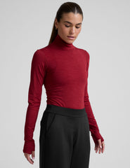 model wearing a red turtleneck long sleeve top and black pants on a plain background.