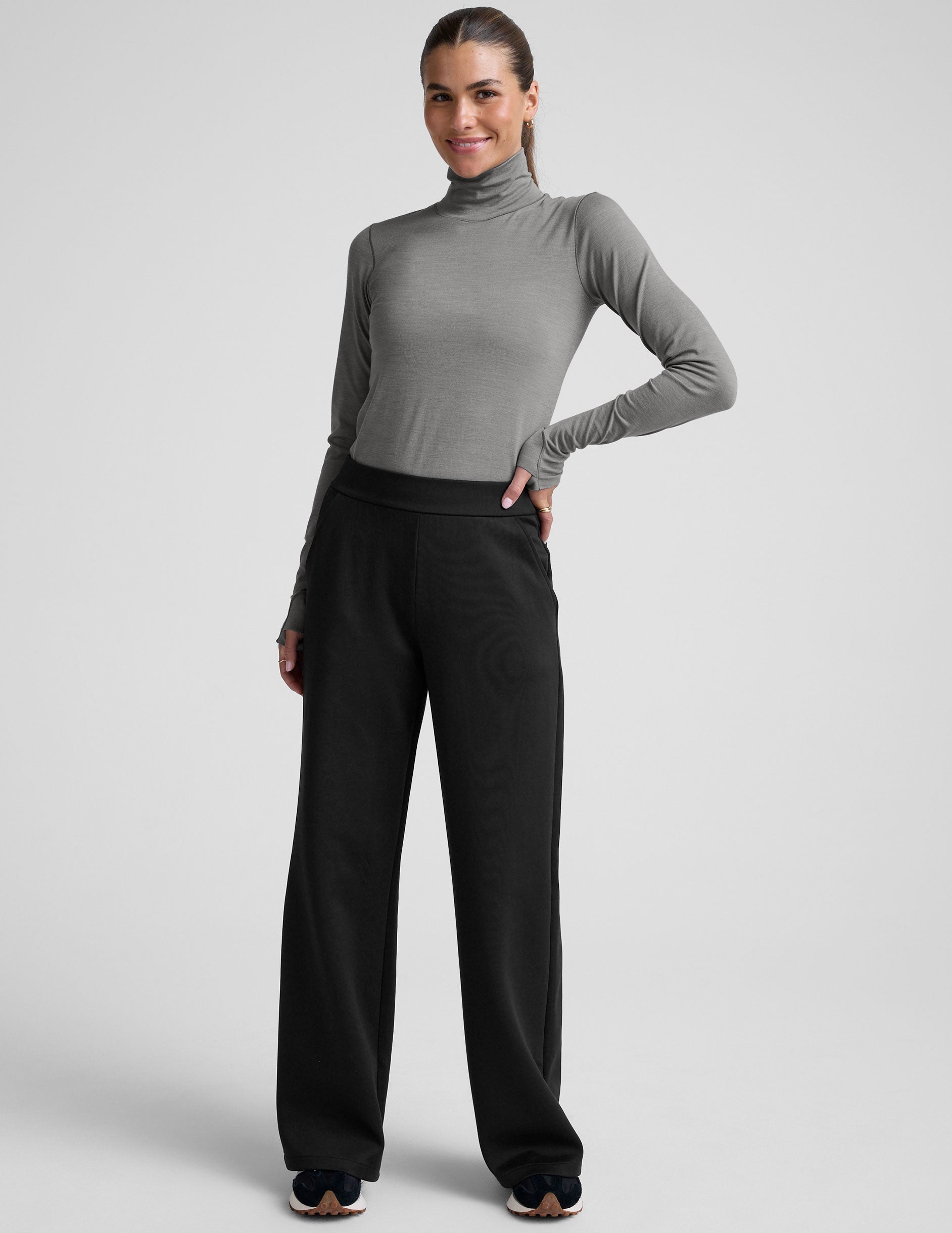 model wearing a gray turtleneck and black pants against a plain background.